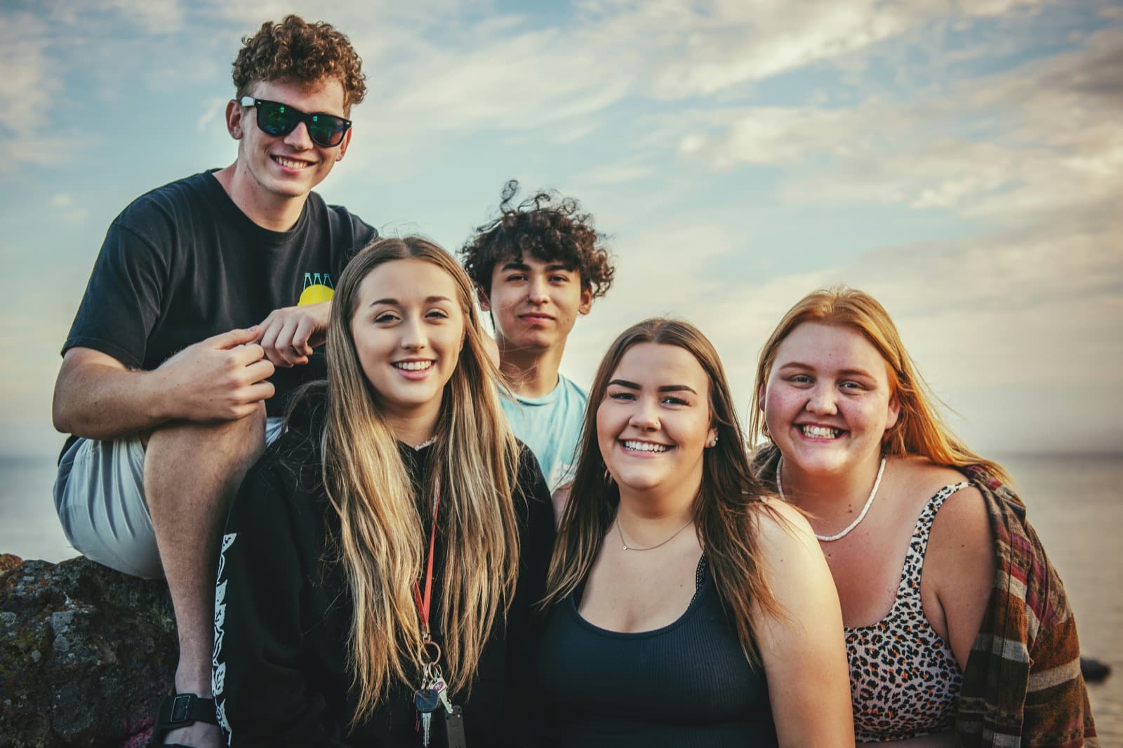 Five teens smiling together outdoors at dusk near the coast