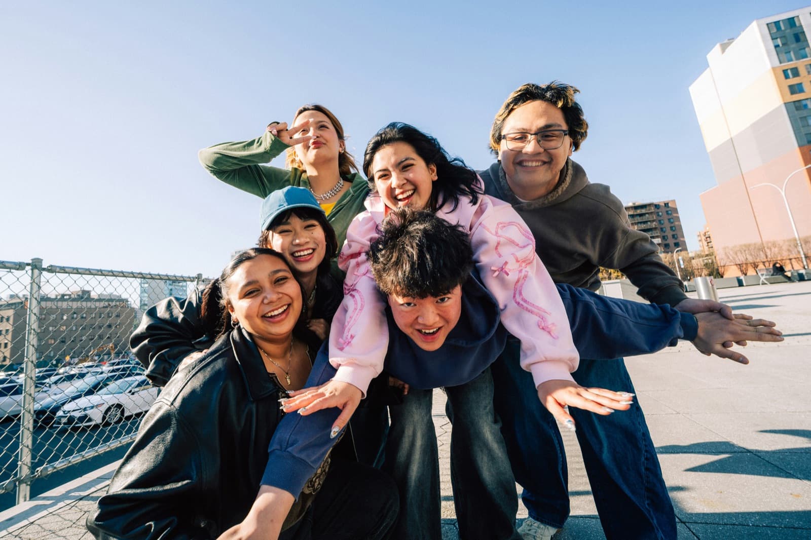 A group of six friends piled together laughing on a sunny rooftop