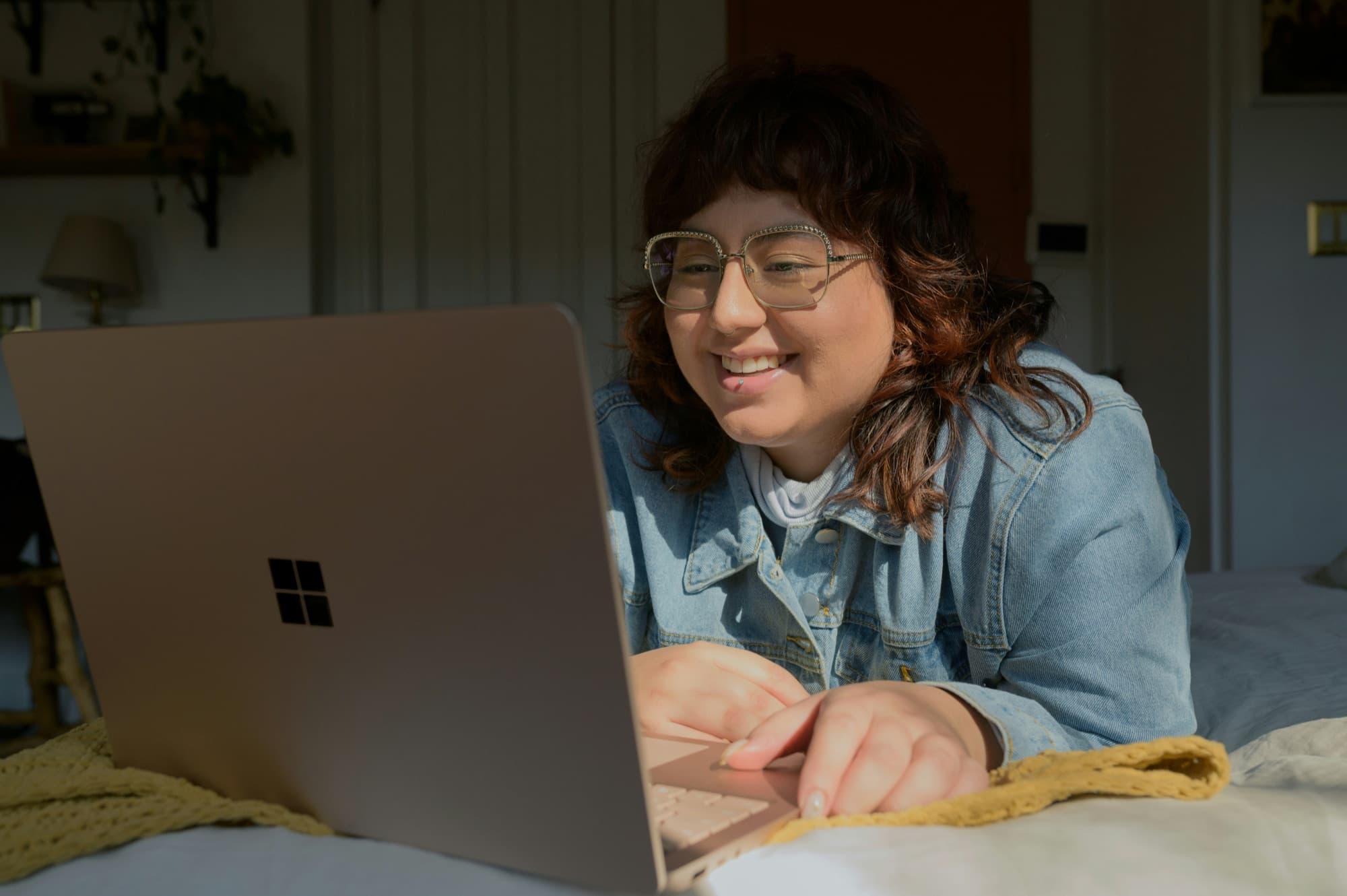 A teen smiling while working on a laptop in bed