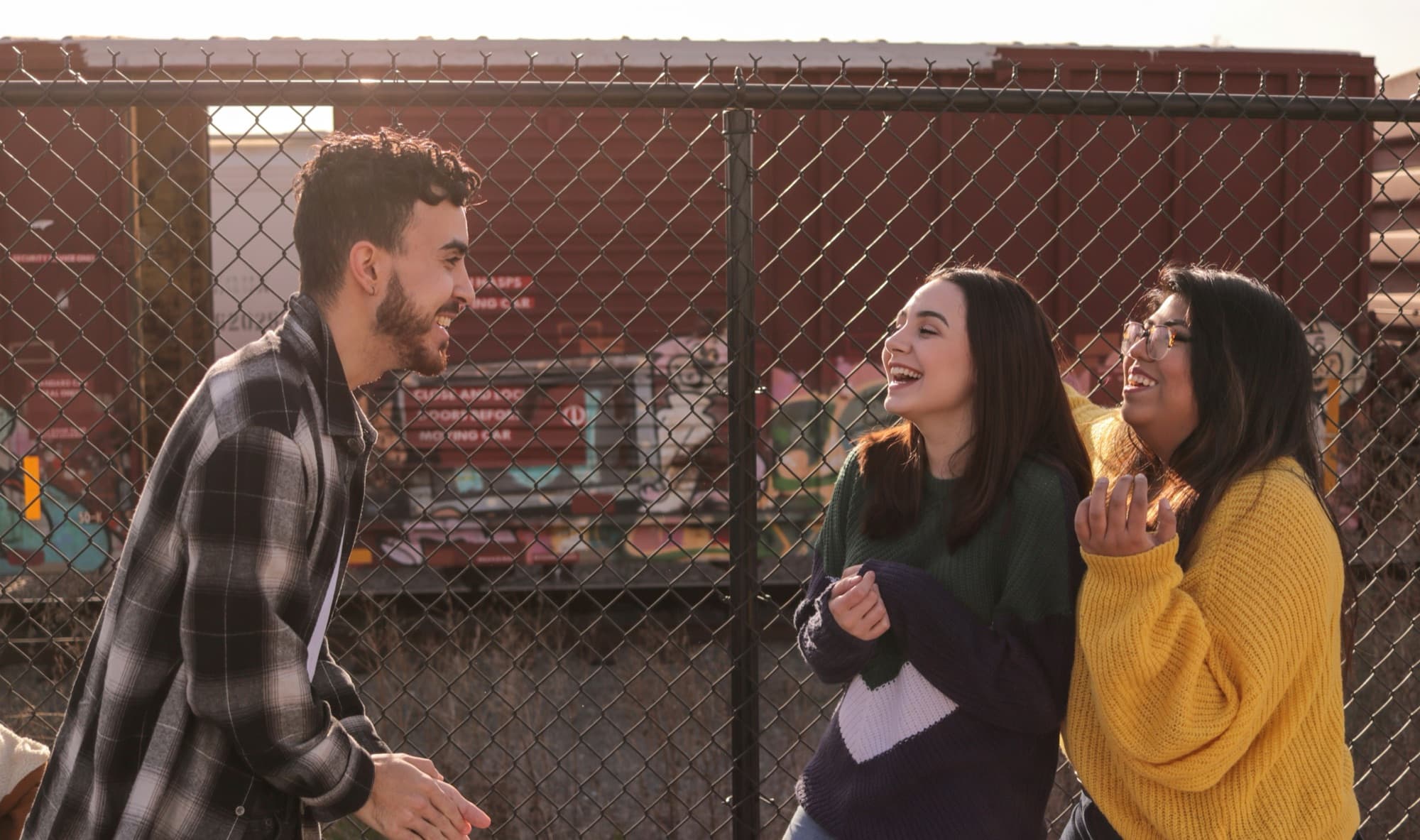 Three teens laughing together by a chain-link fence