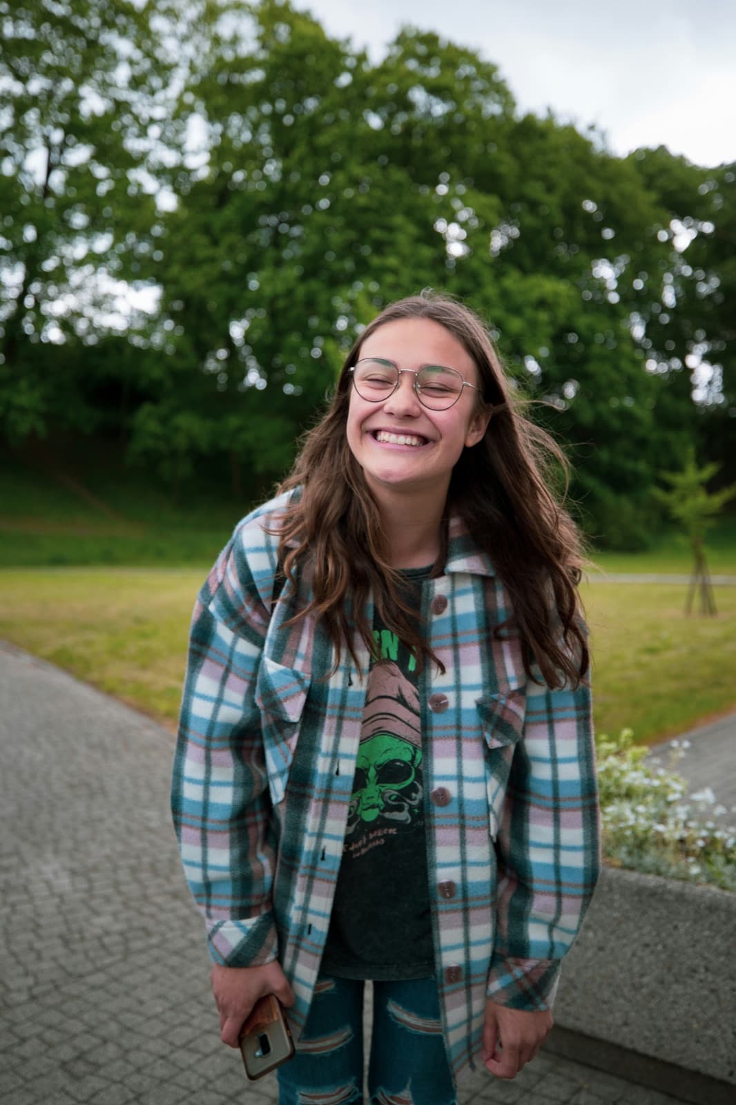 A teen in a plaid flannel shirt laughing outdoors on a park path