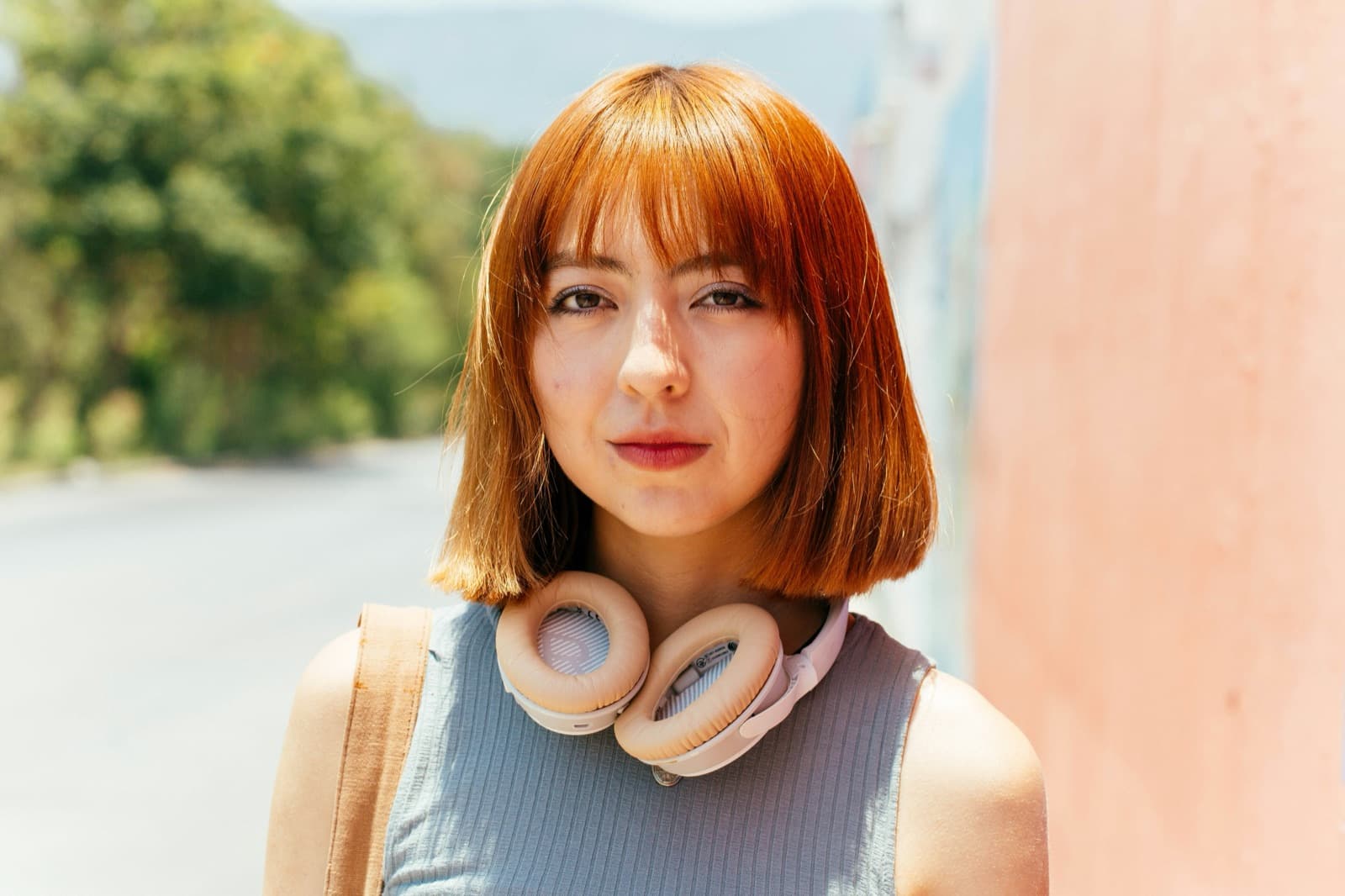 A teen with a short bob haircut and headphones around her neck in warm sunlight