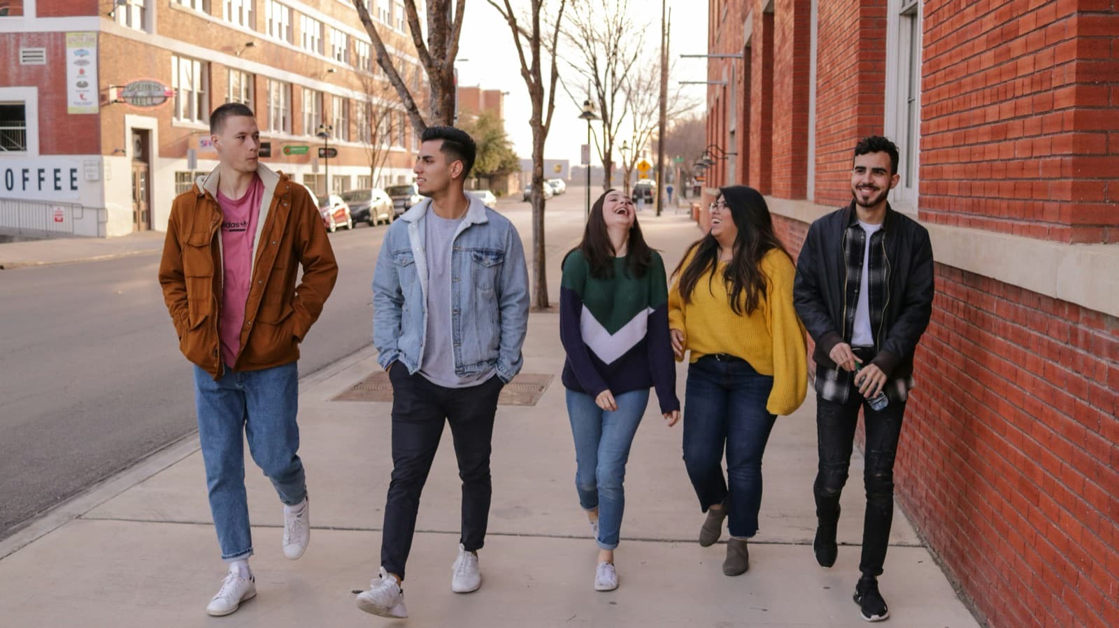 Five teens walking together down a city sidewalk on a sunny day